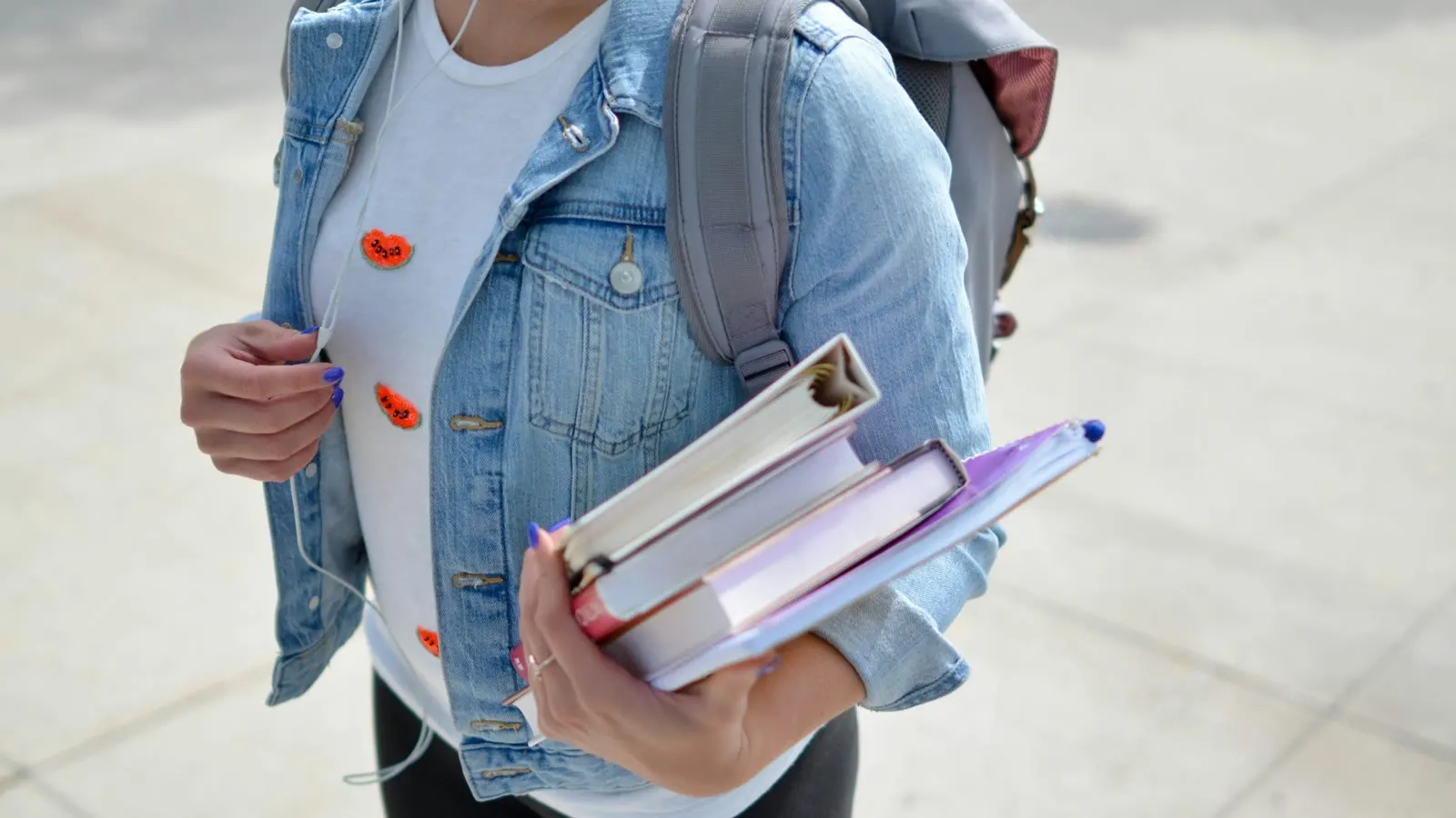 A student carrying books and a backpack outdoors