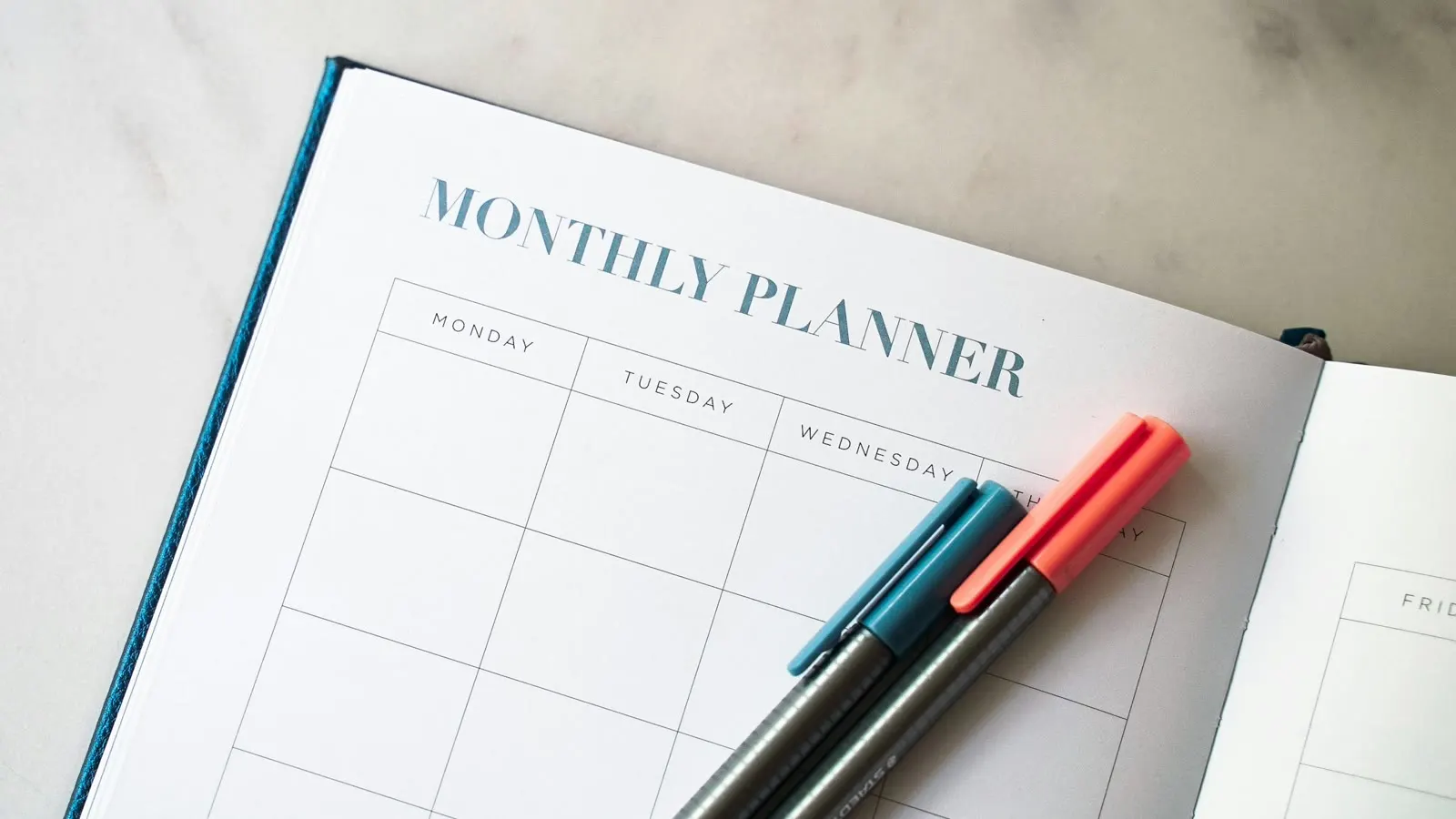 An open monthly planner with colorful pens