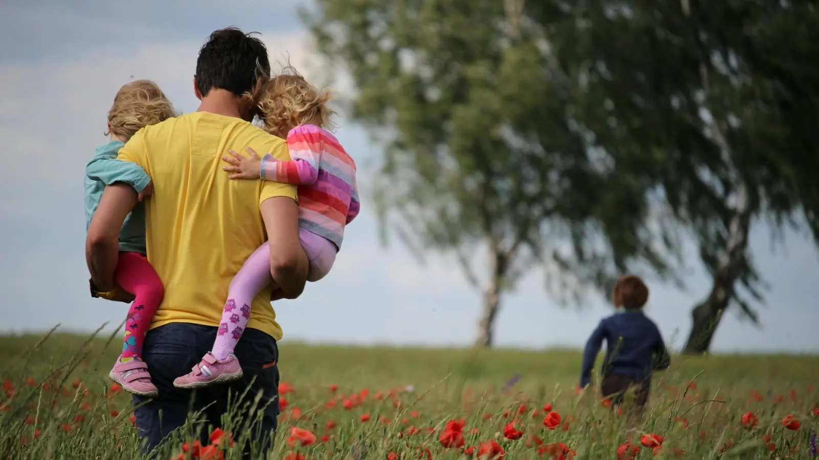 A caregiver carrying a child through a field